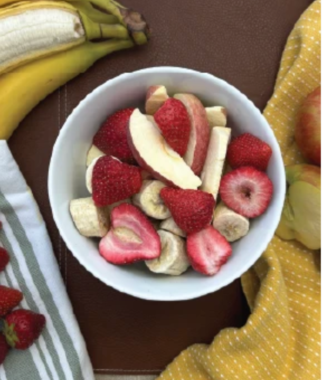 A bowl of Fresh Dry fruit snacks surrounded by whole fruit